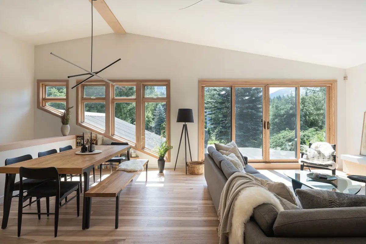 Dining table and sofa under a vaulted ceiling, wood framed windows onto forest and mountain