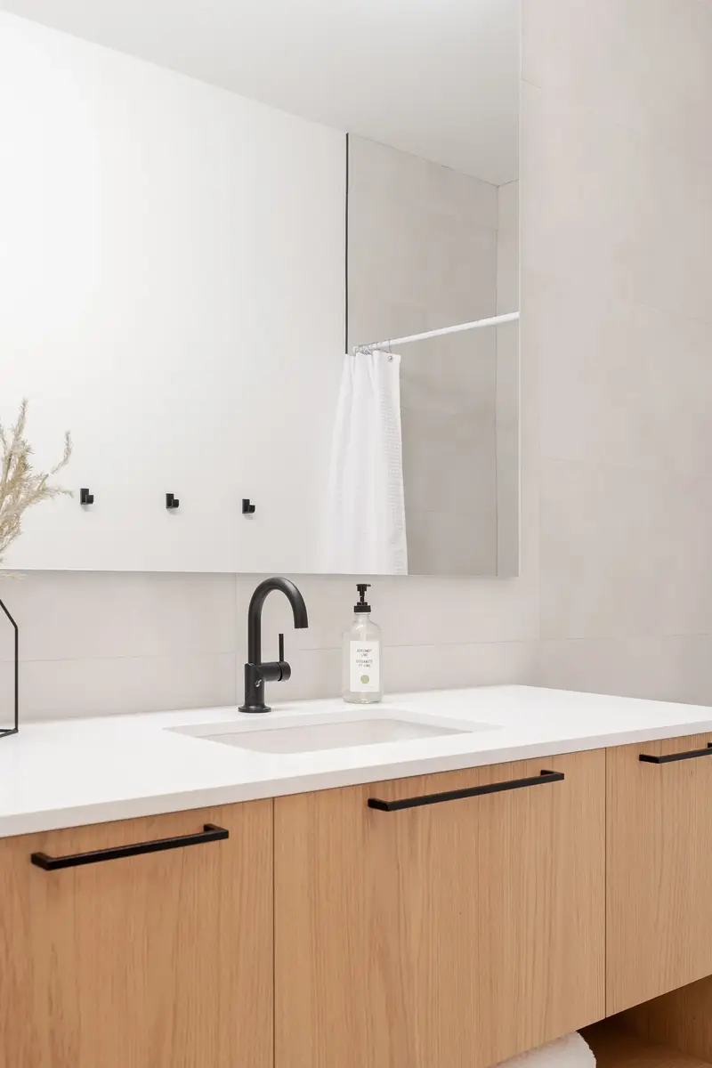 Undermount sink and black tap on a white counter, mirror reflecting a curtained shower
