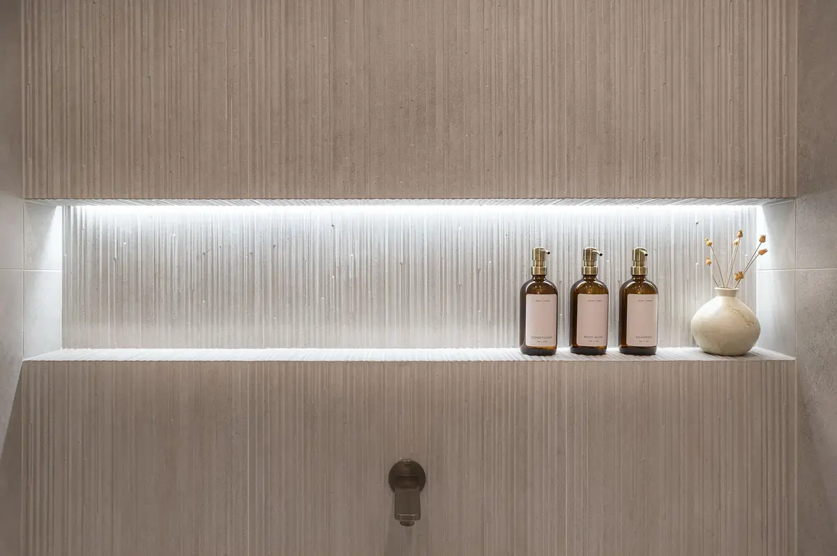 A lit recess in a ribbed wall holding three bottles and a small vase