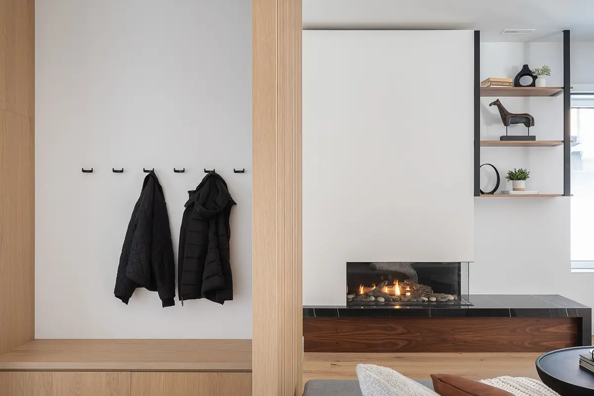Entry bench and black wall hooks holding two dark coats, a lit fireplace beyond