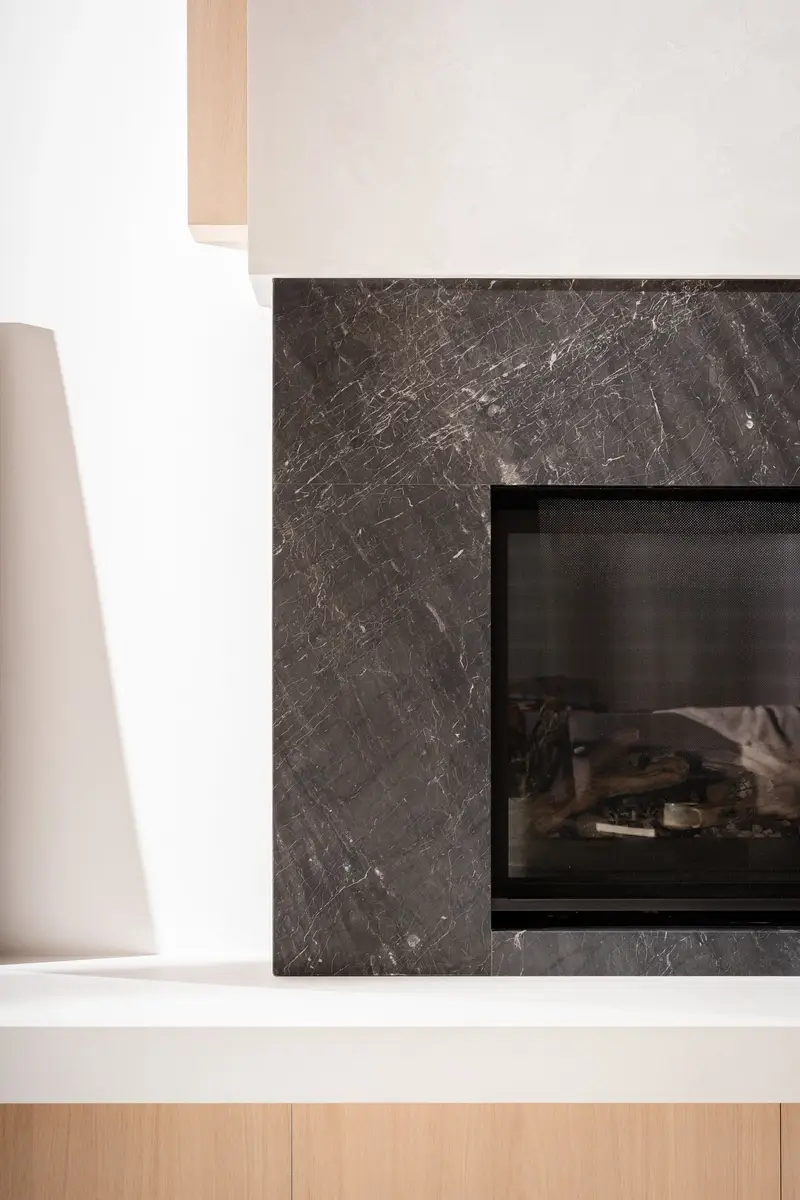 Firebox in a dark veined slab beside white plaster, a wood bench running below