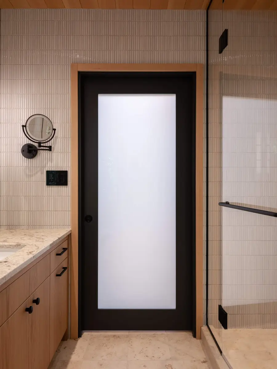 Bathroom in fine ribbed tile with a black framed frosted door and a round mirror