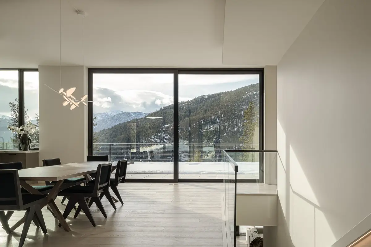 Dining table and chairs under a branching pendant, full height glazing to the mountains