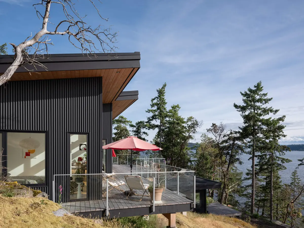 Oles Cove, Halfmoon Bay, dark corrugated cladding and a deck with a red umbrella above the ocean