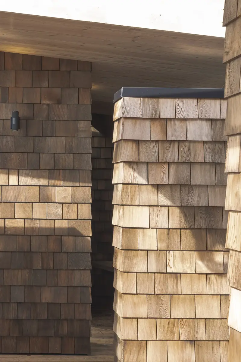 Two shingled volumes meeting at a narrow slot, light and weathered shingles side by side