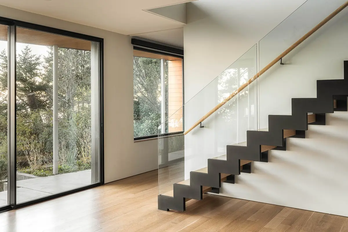 Entry hall with a steel stair and glass balustrade, sliding glass to the trees