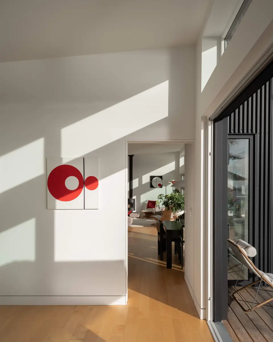 Shadows raking a white wall, a doorway through to the dining room and deck