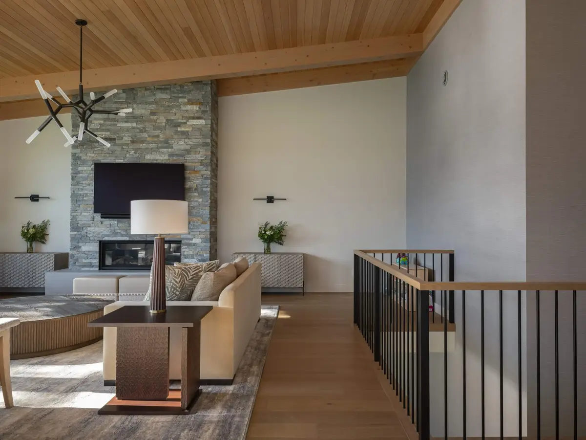 Living room under a wood ceiling, a stone fireplace ahead and a black railing at right