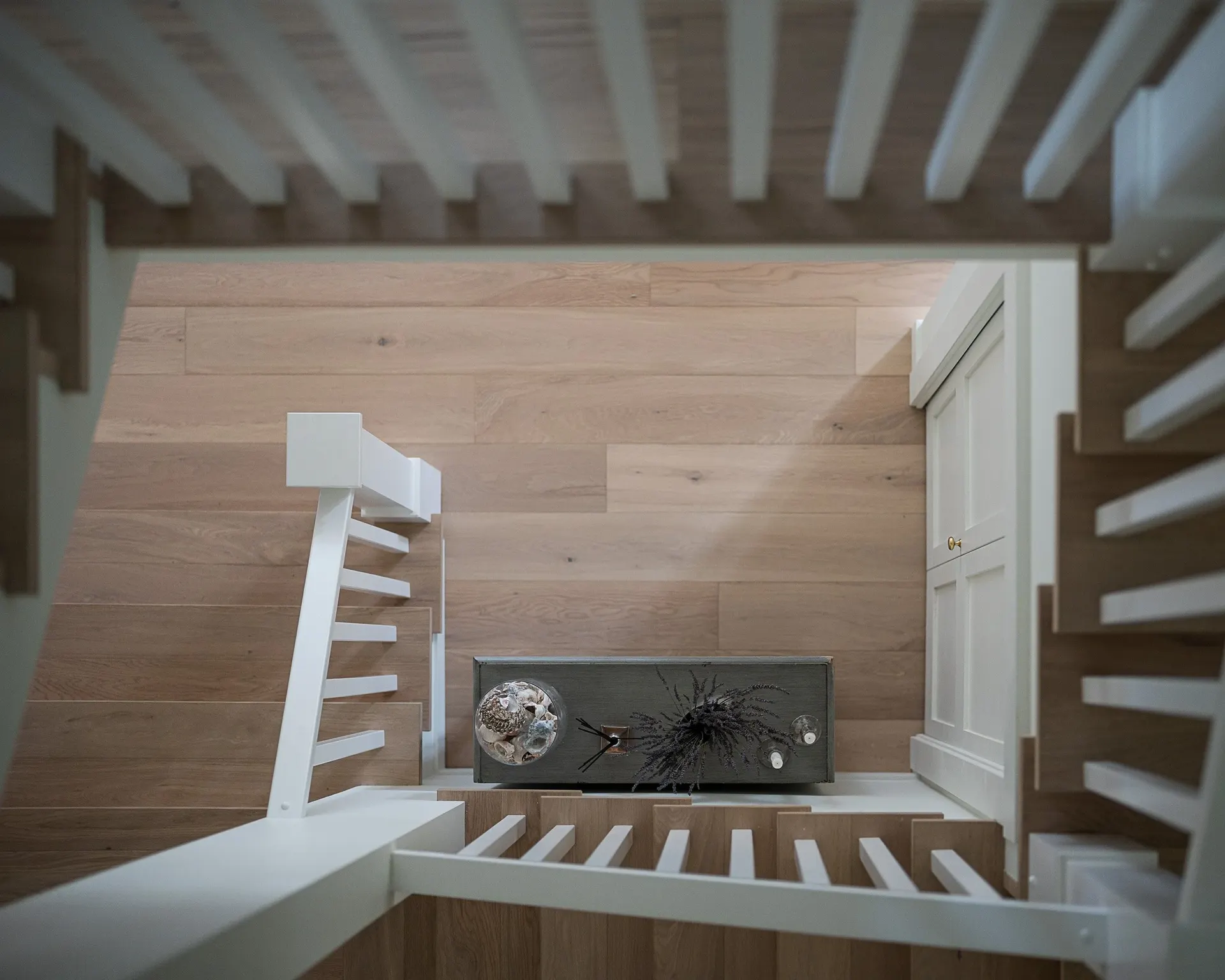 Looking down the stairwell to a landing, a console with dried flowers below the flight