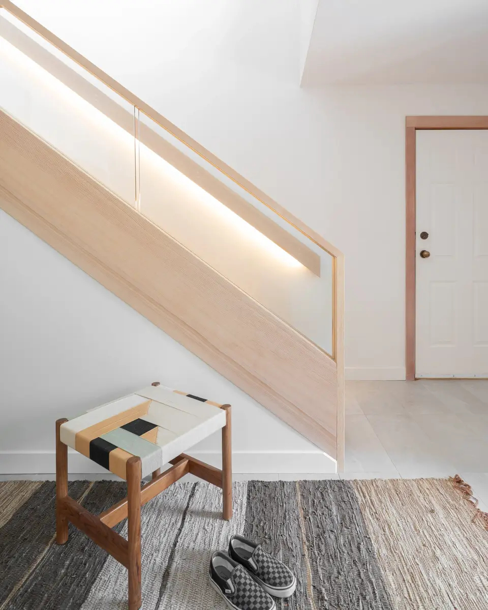 Stair with a lit handrail above a bench and a striped rug in the entry