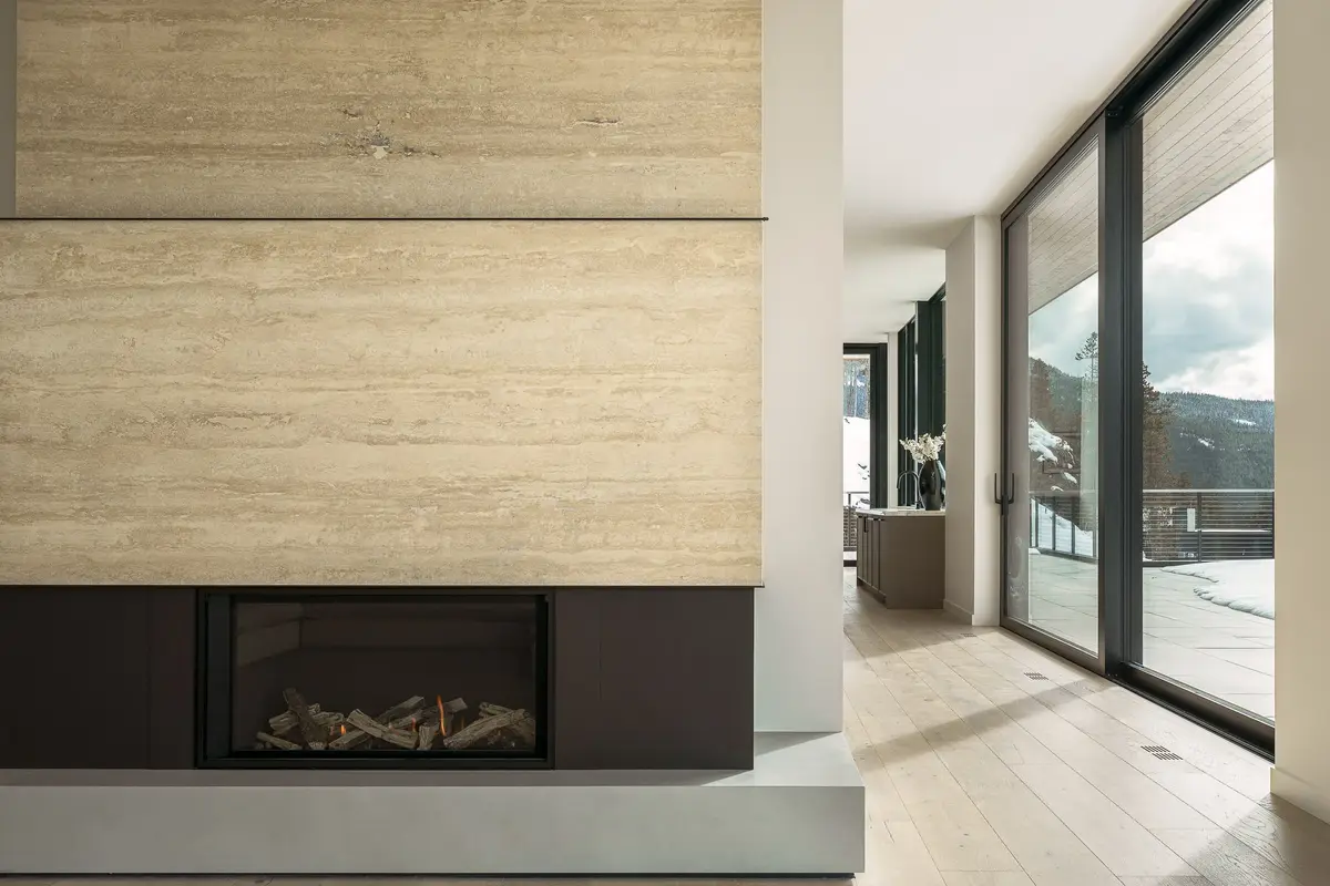 Fireplace wall in pale veined stone above a dark firebox, the room opening to the terrace