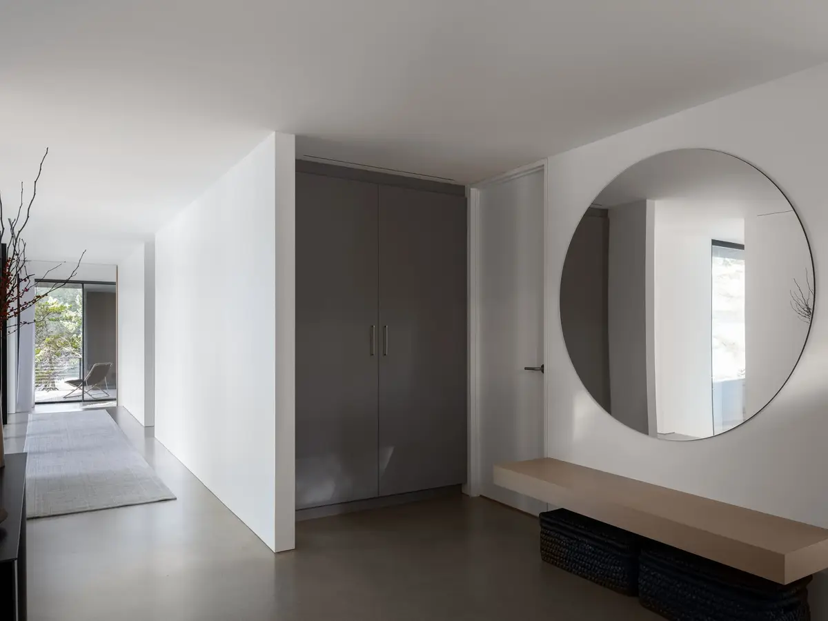Hall with a large round mirror above a floating bench, tall doors and baskets below