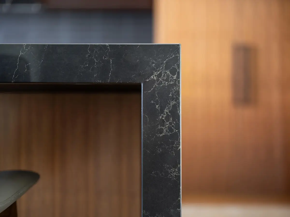 Island end in dark veined stone falling to the floor, warm wood cabinetry behind