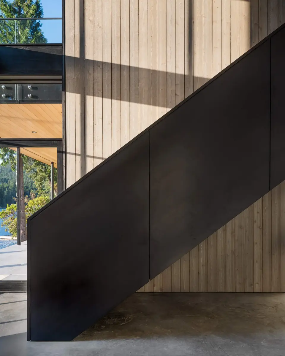 A dark steel guard cutting diagonally across a pale board wall in raking sun