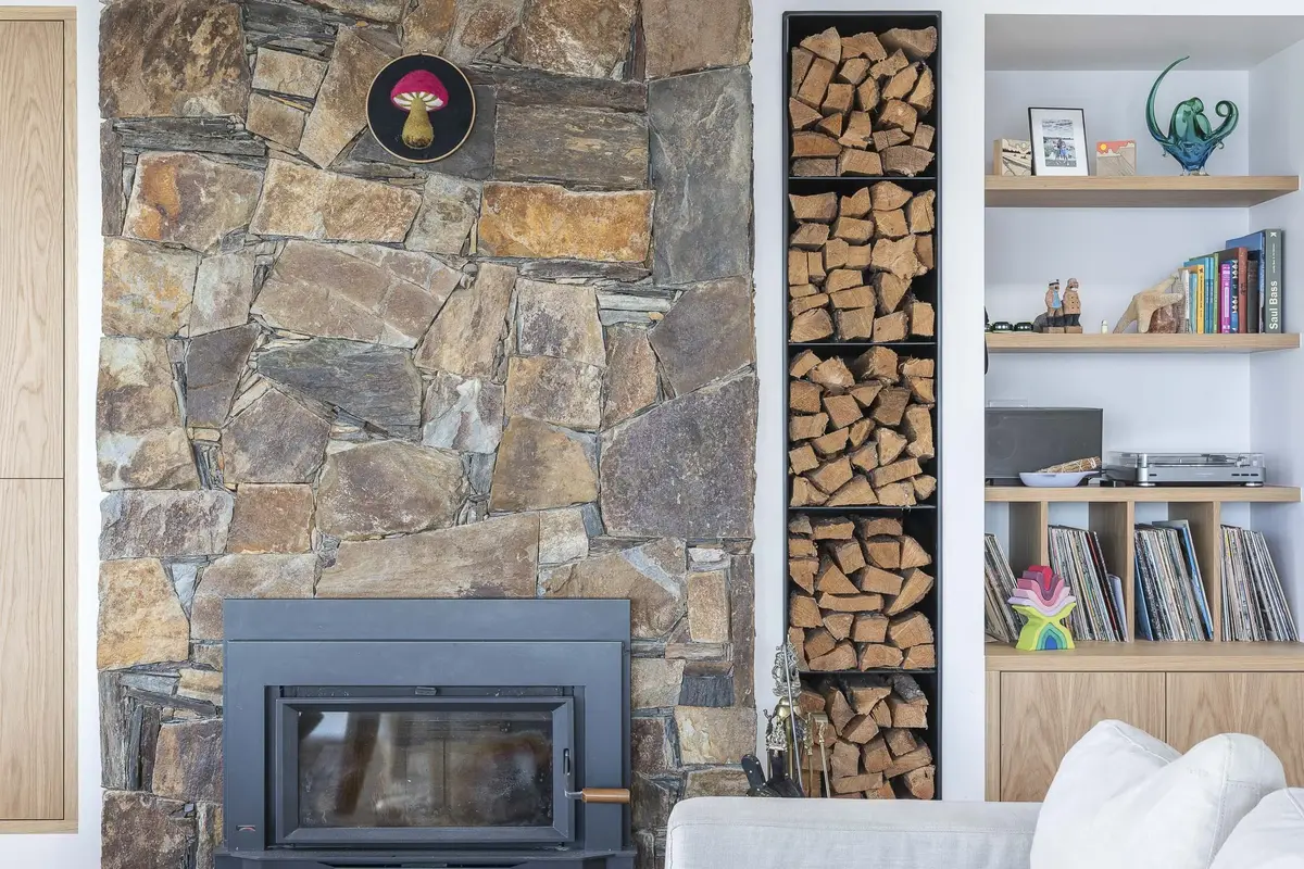 Stone chimney and black firebox beside a stacked firewood niche and shelves of records