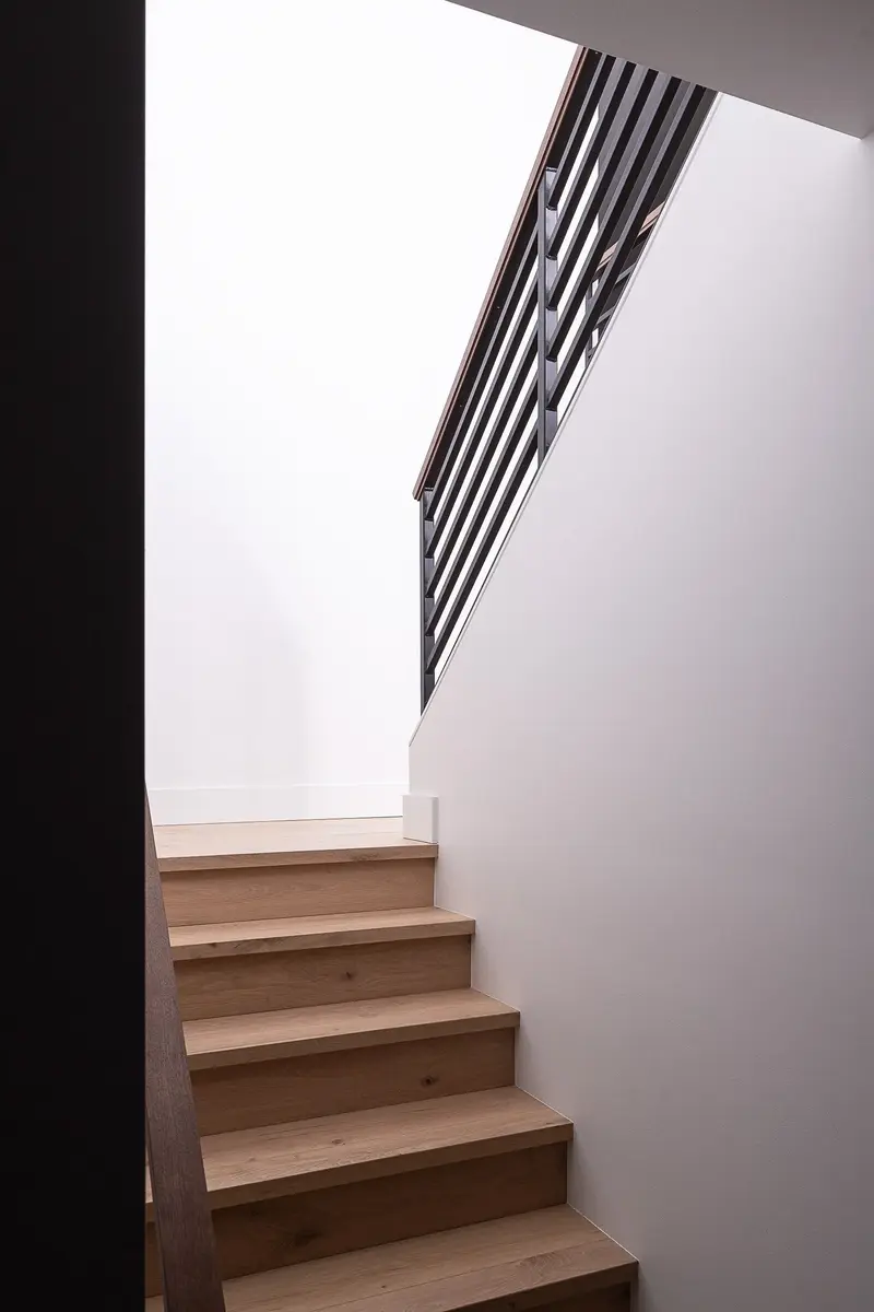 Wood stair treads rising against a white wall, dark metal balustrade above