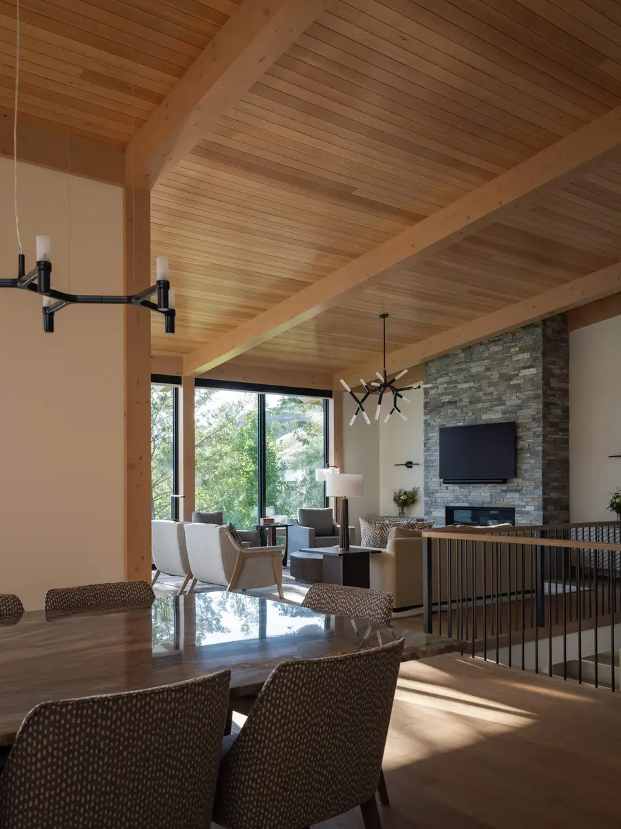 Dining table and chairs under a black light fixture, living area and fireplace beyond a railing