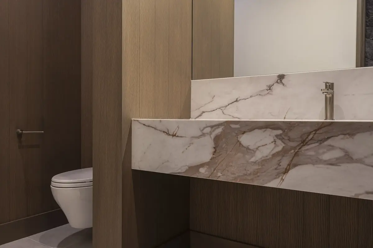 Powder room with a veined stone counter folded down over dark cabinetry, wall hung toilet beside