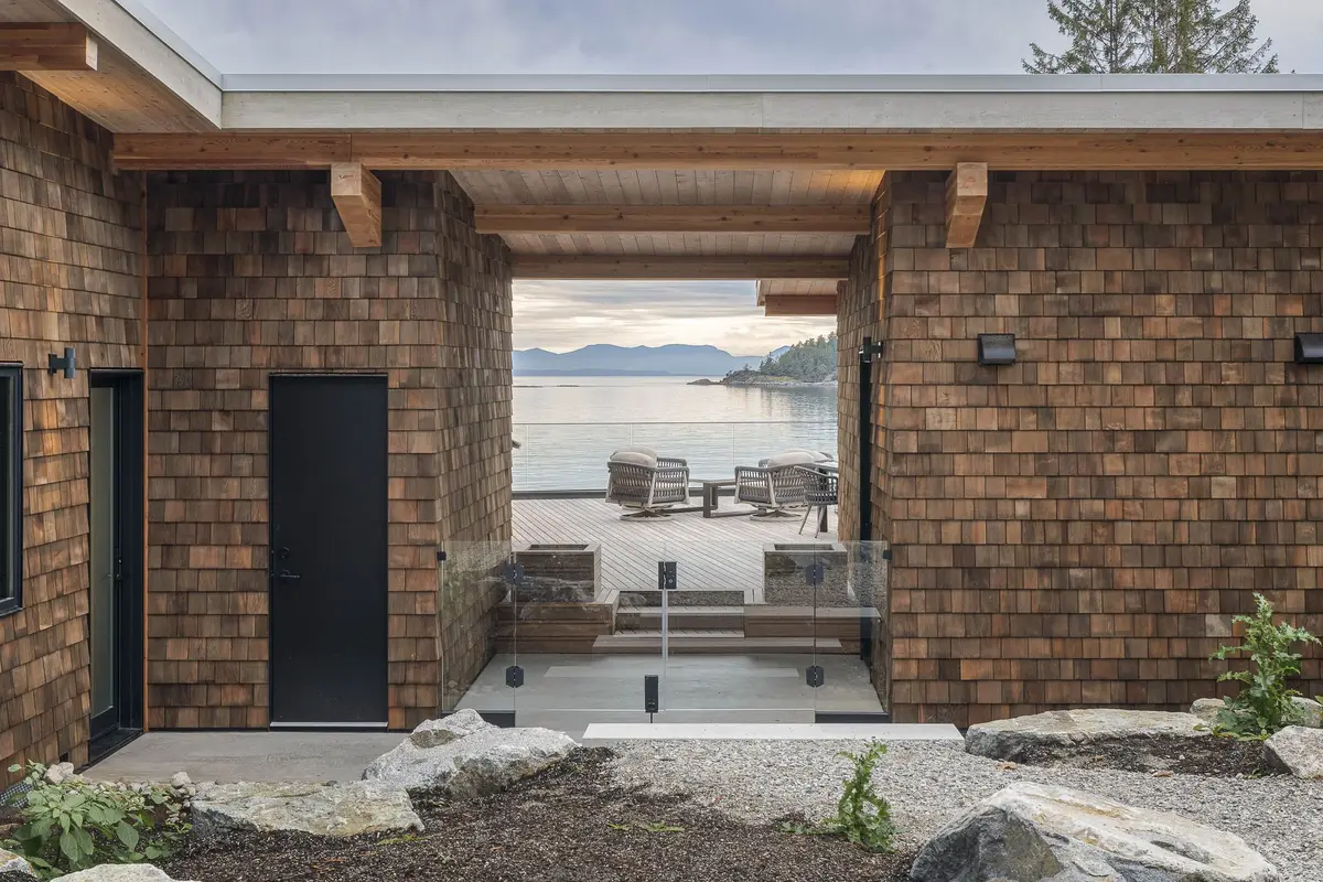 A covered opening between shingled walls framing deck chairs and the water beyond