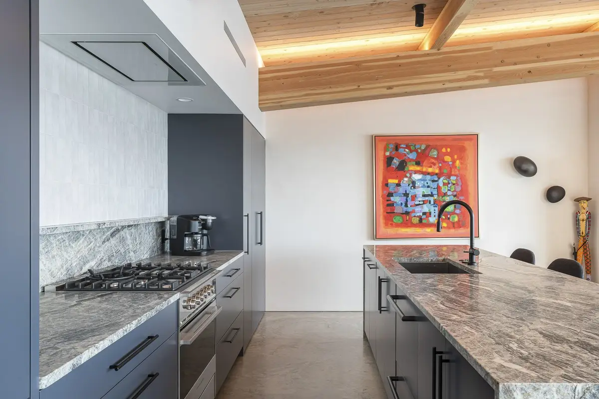 Range and stone counter along the kitchen wall, island and framed artwork beyond