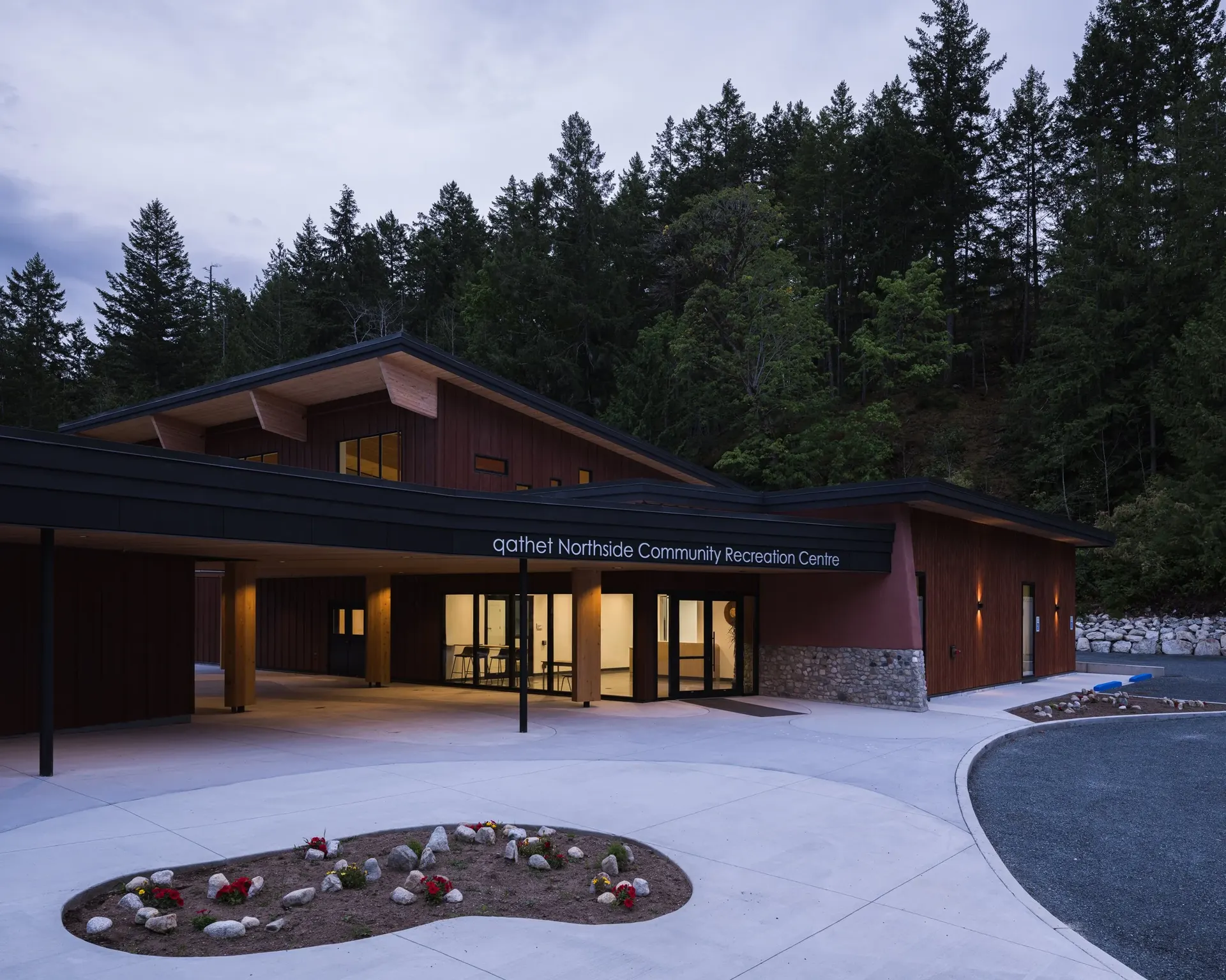 The entrance at dusk, warm light through the lobby glazing and the planted court in front