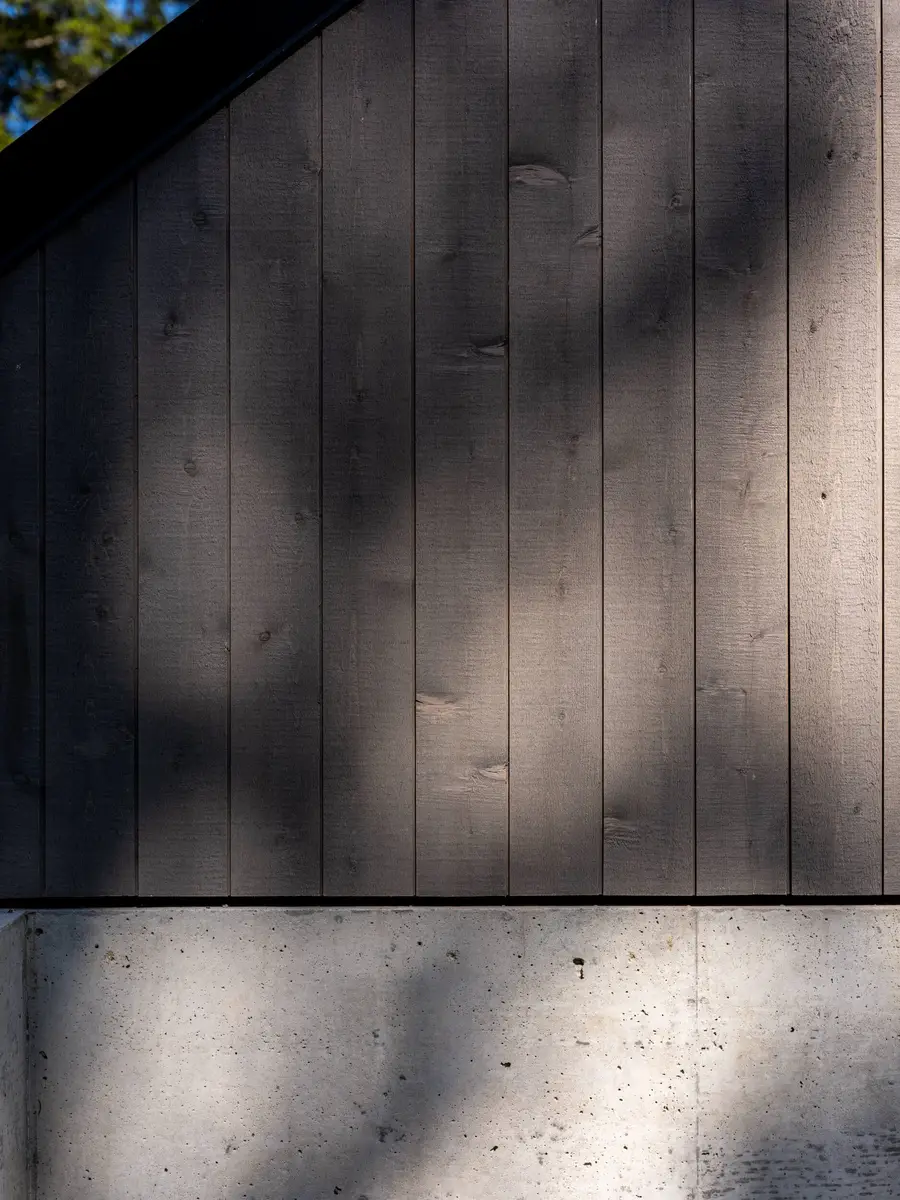 Dappled light on dark boards where they meet the concrete below, gable edge above