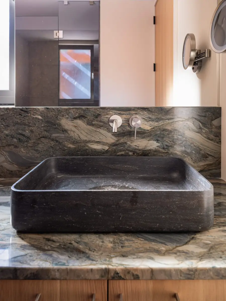 Dark stone basin on a heavily veined counter with a wall mounted tap above