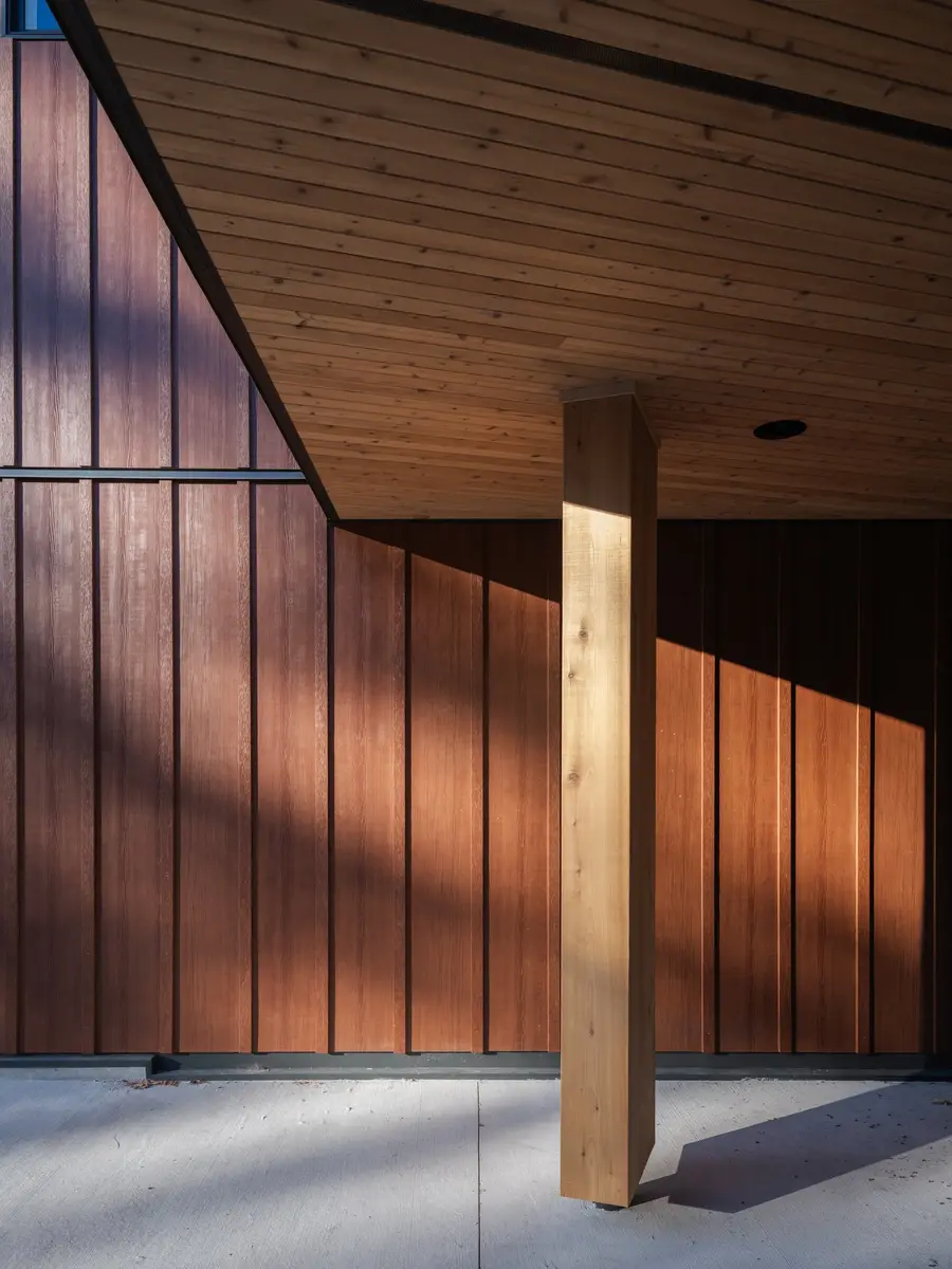 A timber column under the covered walk, low sun raking across the cladding