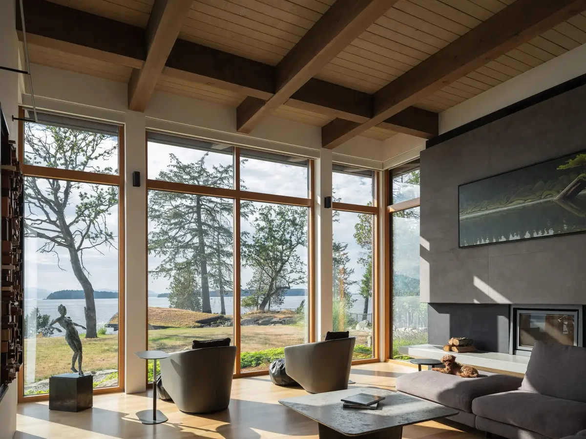 Living room under exposed beams, full height glazing to the trees and the water