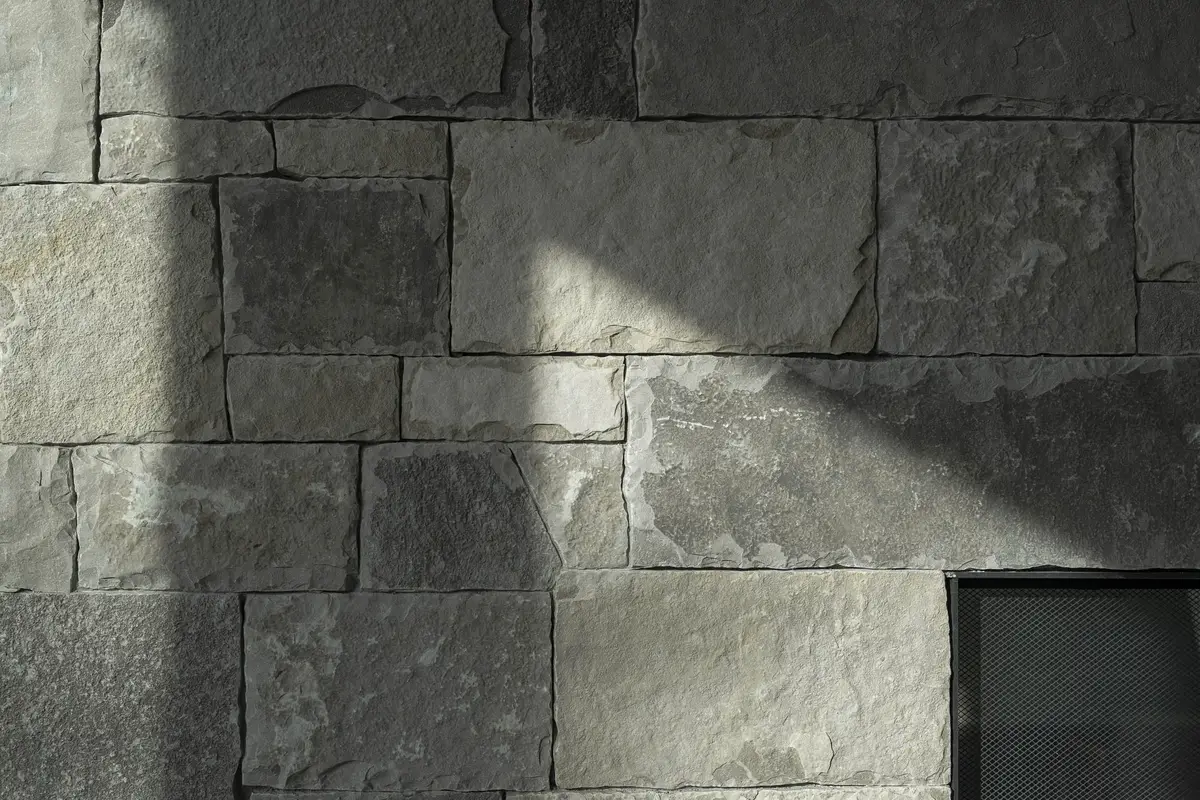 Coursed stone wall in raking light, a band of sun across the blocks