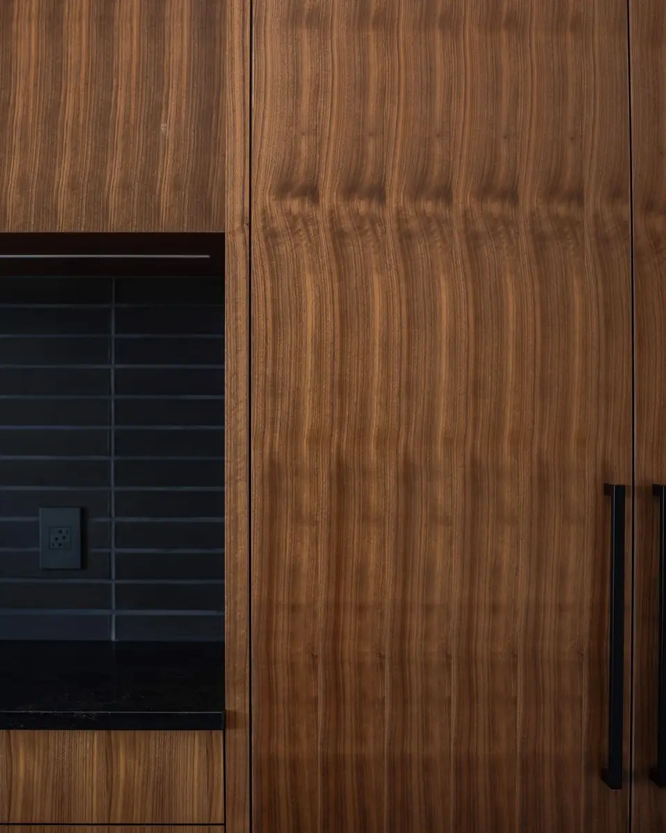 Wood cabinetry above a dark counter, narrow tile running up the wall in shadow