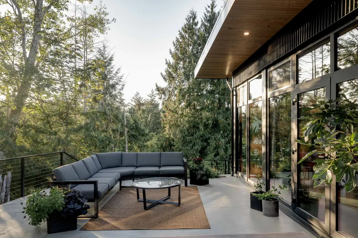 Terrace seating under a wood soffit, glazing at right and treetops falling away beyond a cable rail