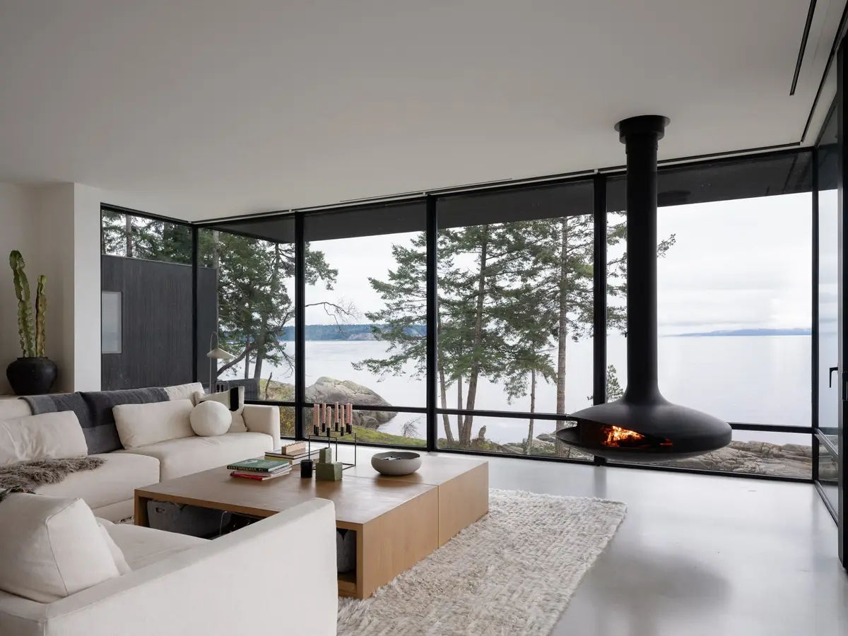 Living room with a pale sectional and low table, the fireplace hanging beside full height glazing
