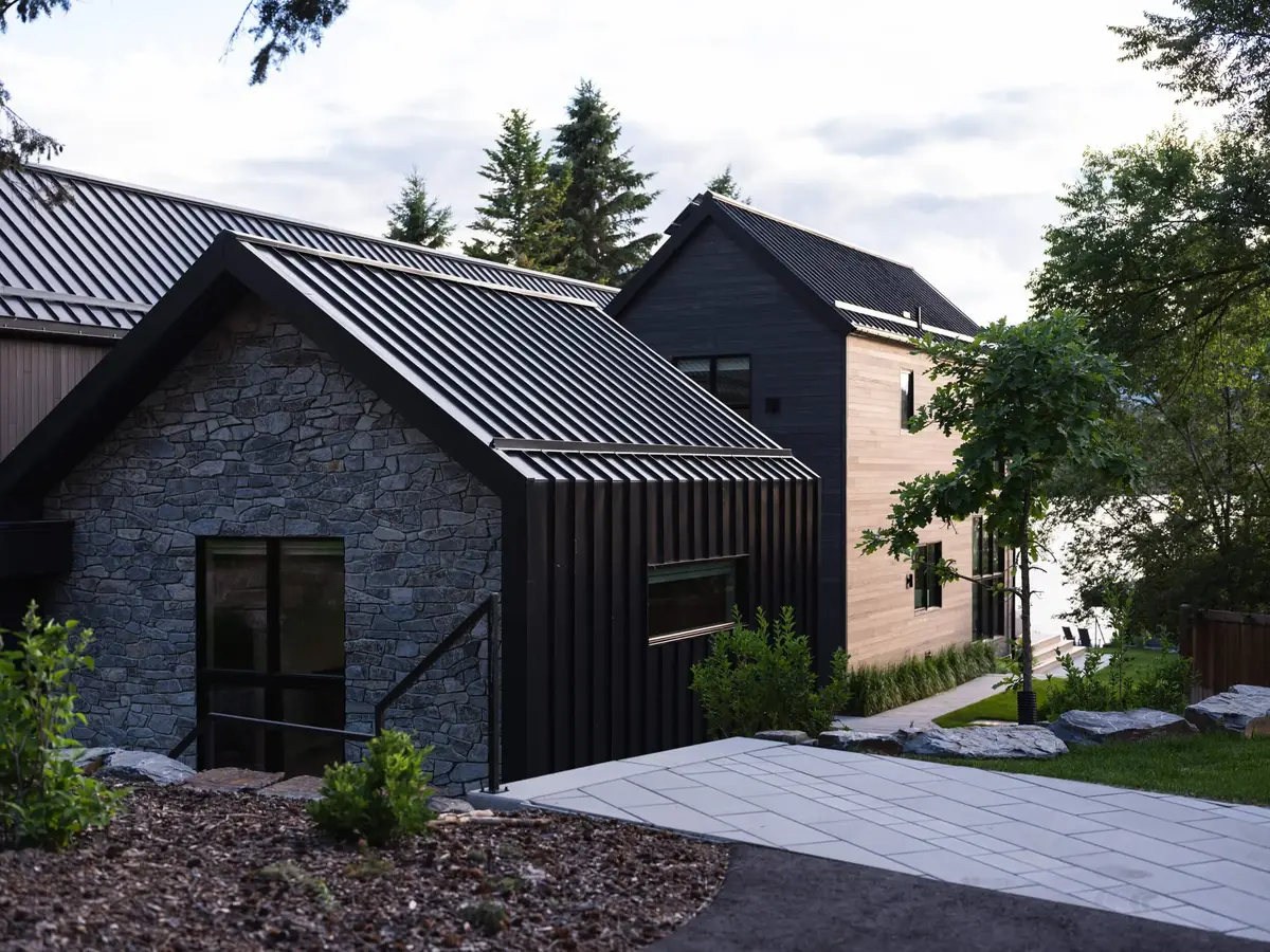 Stone gable under a ribbed dark roof, the lake showing through trees beyond a path