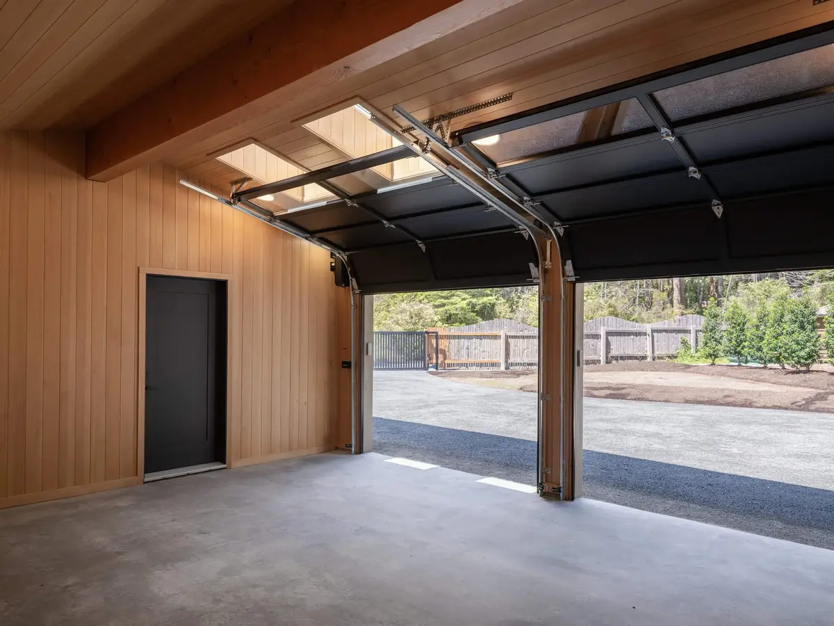 Empty garage with the door raised to gravel and trees, wood lined walls inside
