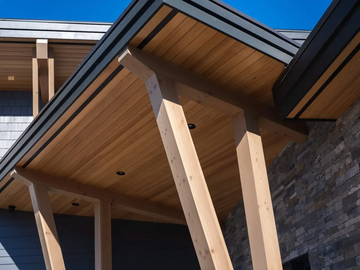 Looking up at a wood soffit and angled roof edge carried on pale timber posts