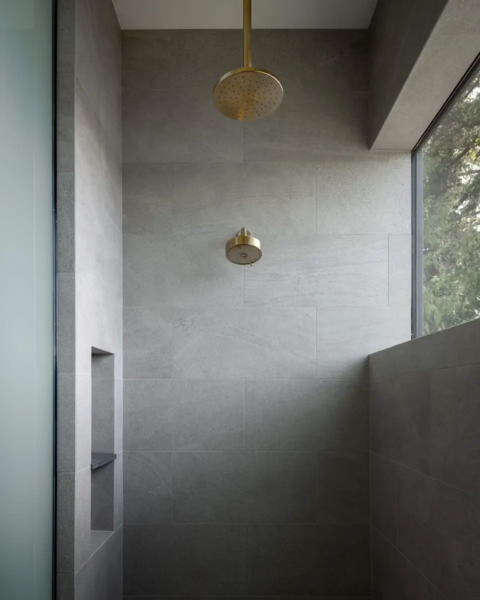 Walk in shower in grey tile, a brass coloured rain head and a window at the right