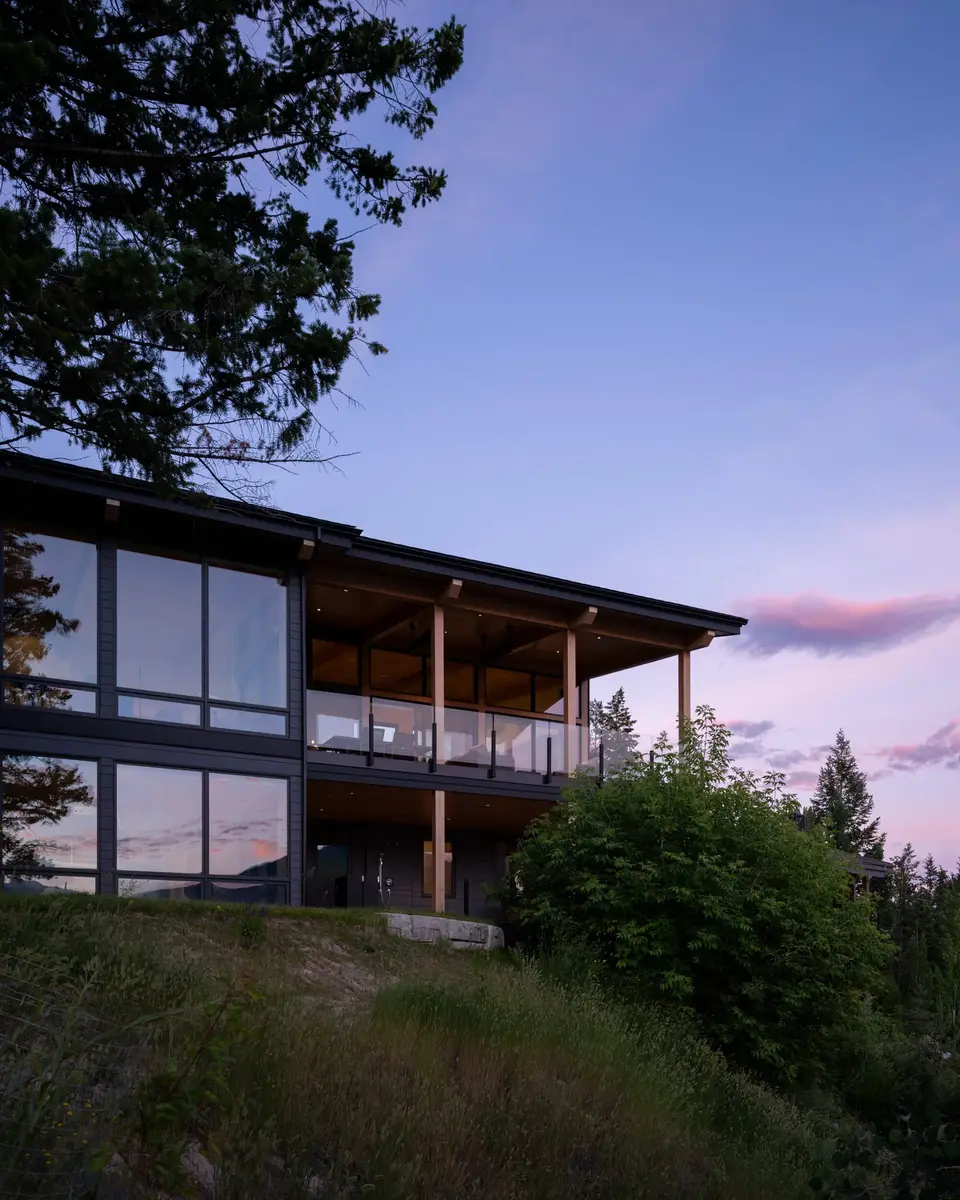 The house on a grassy slope at dusk, decks lit under a violet sky