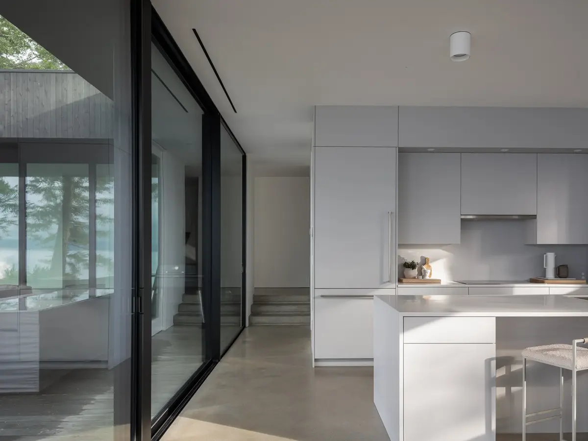 The kitchen seen past a sliding glass wall, concrete steps rising to a landing