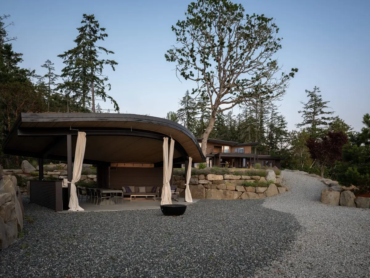 Pavilion and house at dusk, a bare tree rising between them above the gravel court
