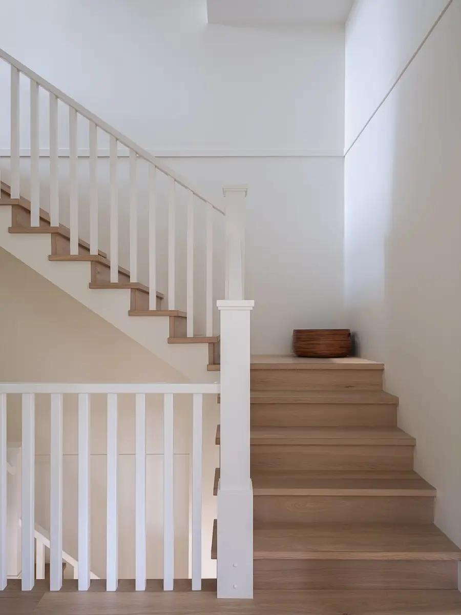Stair rising in wood treads behind white balusters, a wood bowl set on one step