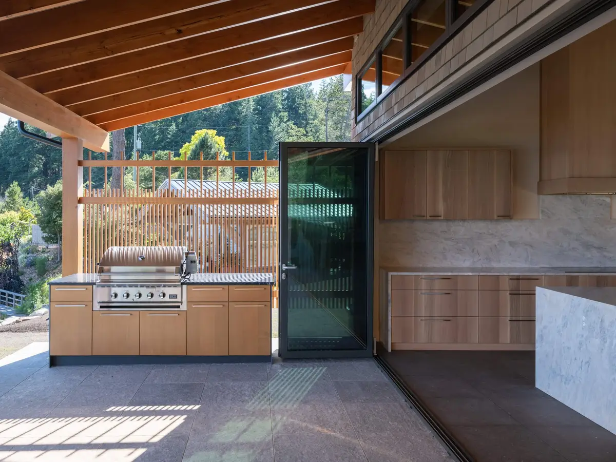 Outdoor kitchen under exposed rafters, a grill set into a stone topped counter