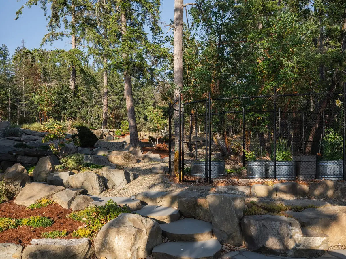 Fenced vegetable garden with metal tanks used as planters among rock walls and steps