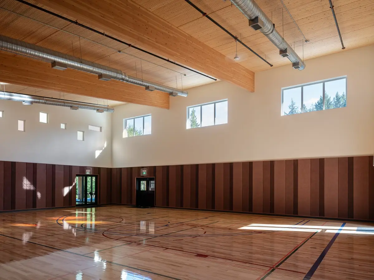 The gymnasium under exposed ducts and timber beams, doors at the far end