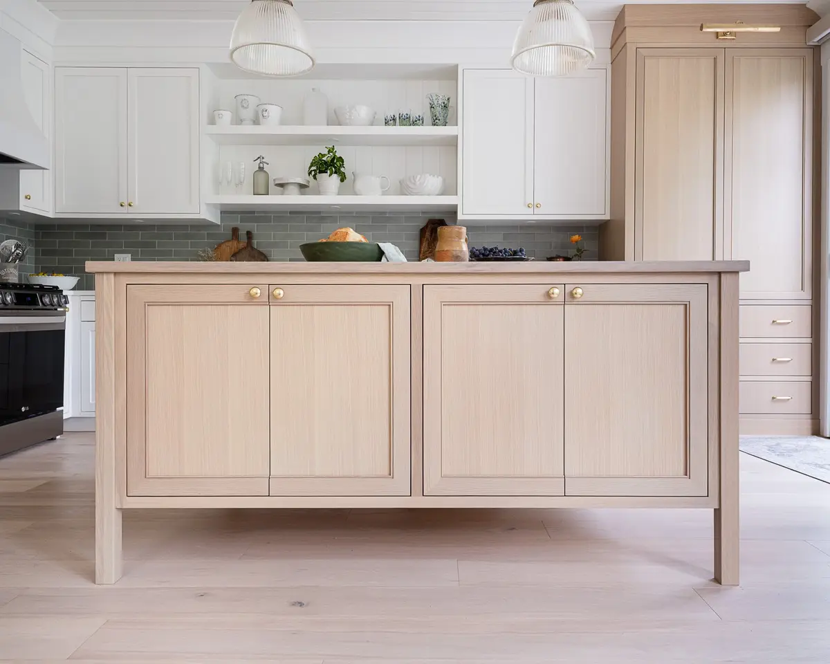 Freestanding pale wood island with gold knobs, the kitchen and a tall cabinet behind