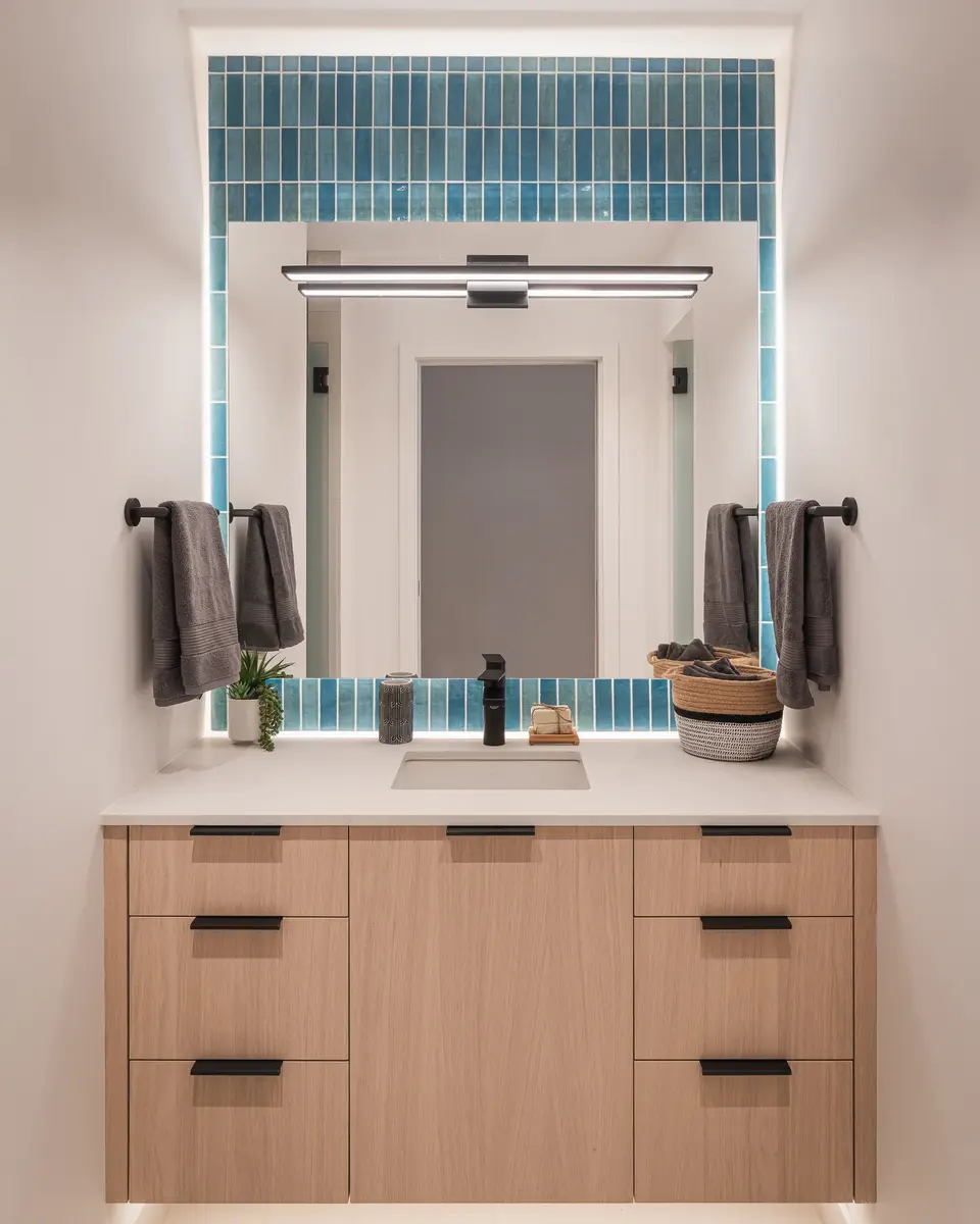 Vanity below a lit mirror, blue tile framing the recess and towels either side