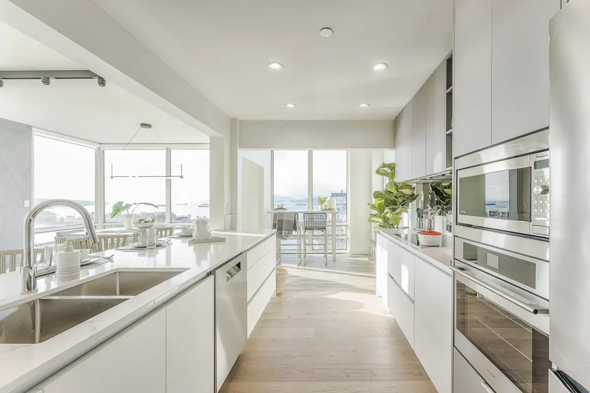 Galley kitchen in white with a long veined counter, ovens at right and water beyond