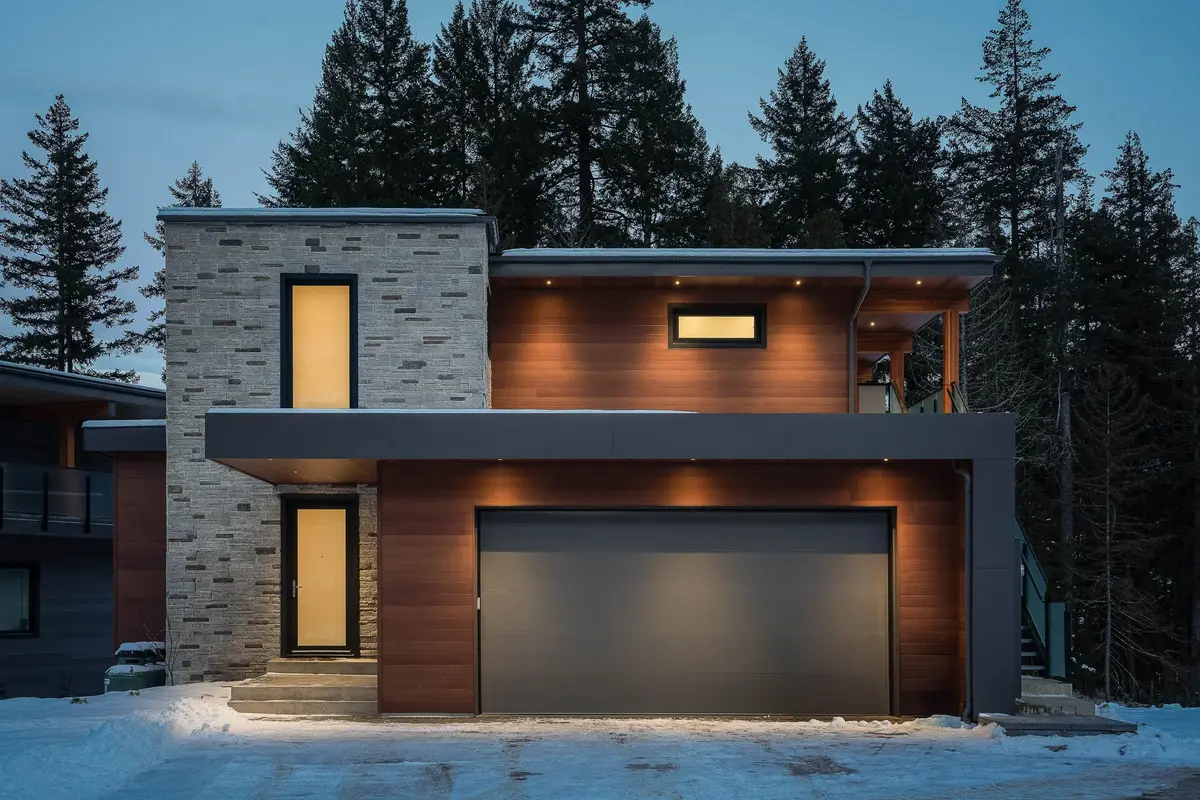 Front elevation at dusk, tall windows glowing and warm light under the deep overhang