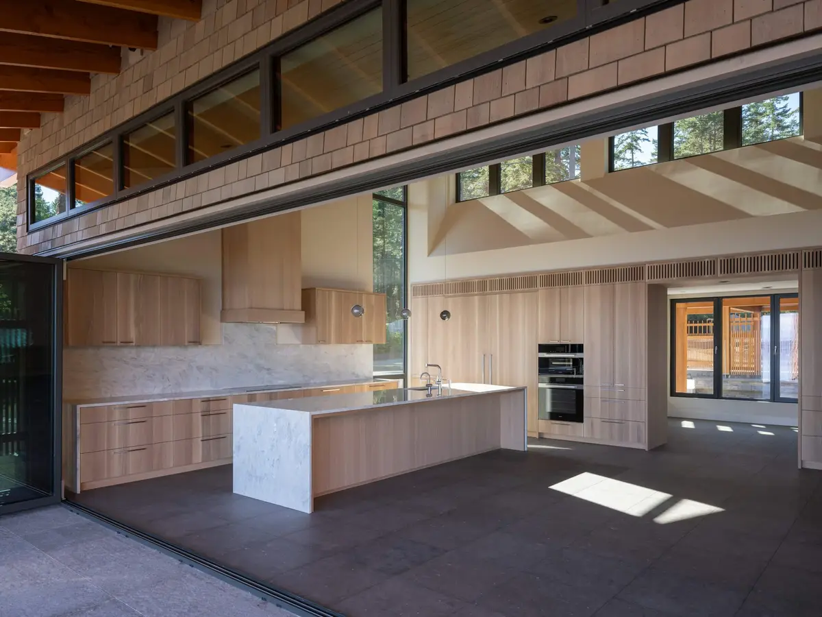 The kitchen seen through a wall of glass slid fully open, clerestory windows above