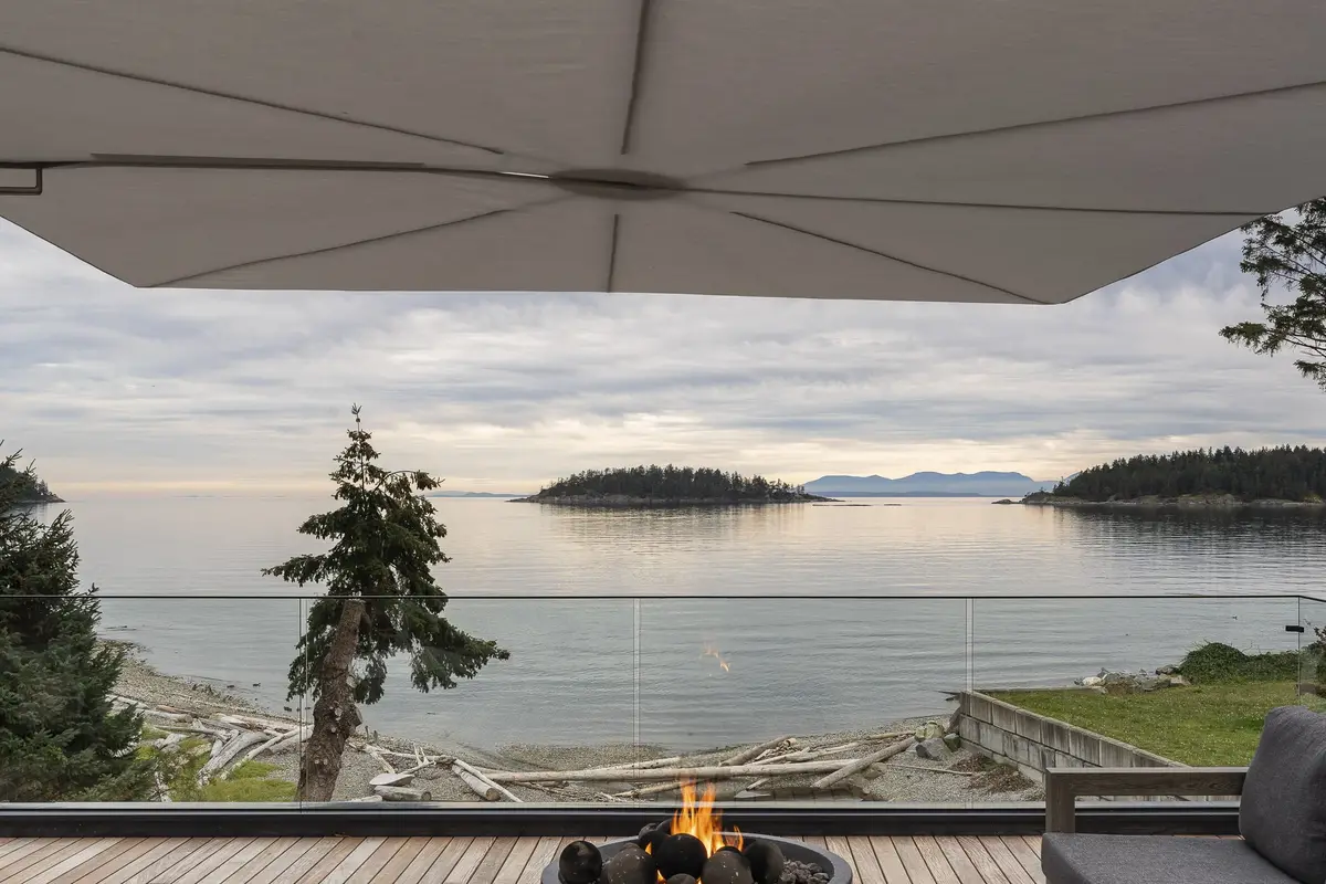 A lit firepit on the deck under an umbrella, islands and calm water beyond